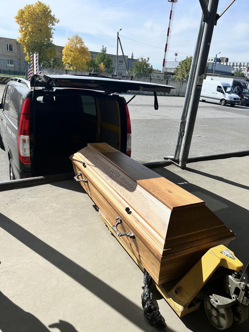 Дерев'яна труна на візку біля ритуального автомобіля