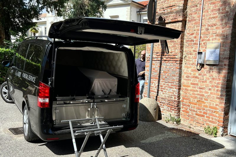 Ритуальний мікроавтобус біля будівлі — передача урни родині після прибуття з-за кордону